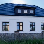 Zewnętrzny widok na elegancki dworek Biała Dama w Gnieźnie, z klasyczną architekturą, dużymi oknami i efektownymi gzymsami otoczony kamiennym ogrodzeniem